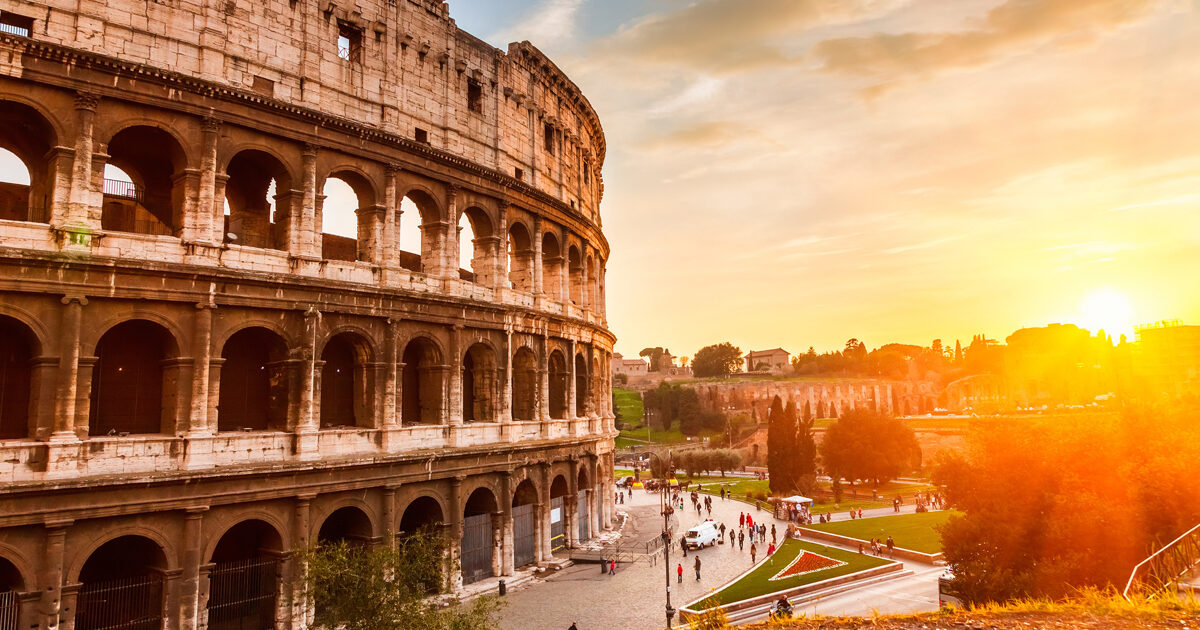 A side view of the impressive Colosseum in Rome with a sunset in the background.